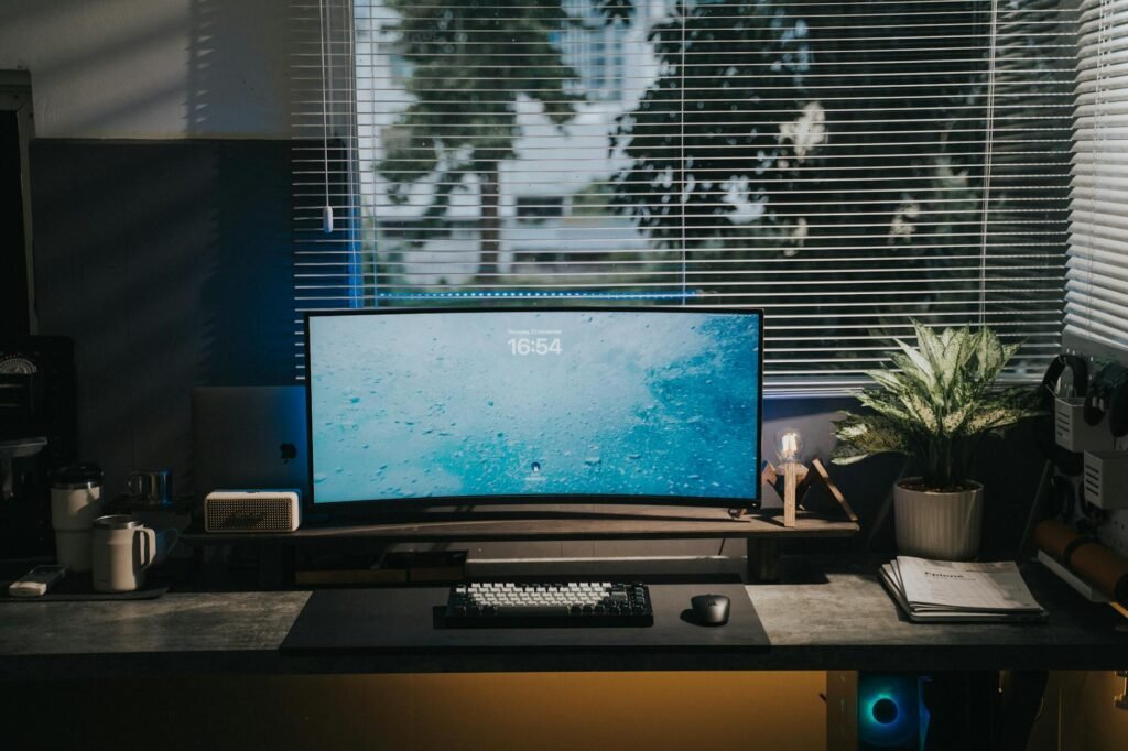 A desk near a window with blinds adjusted to prevent glare on the monitor.