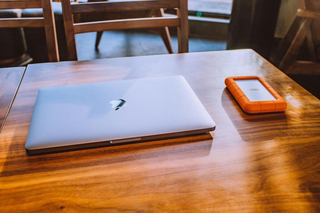 A new laptop on a desk next to a receipt, notebook, and external backup drive.