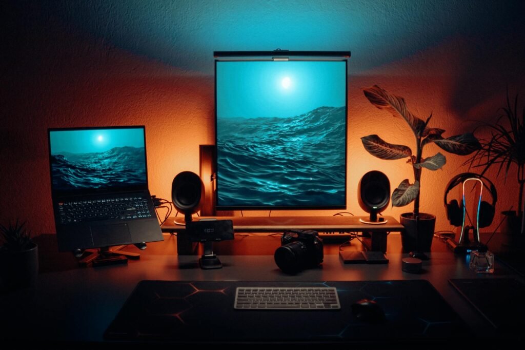 A work laptop on a stand beside a desktop monitor and webcam on a shared desk