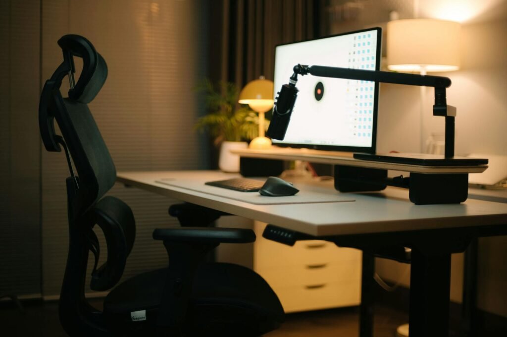 A simple home office desk with one monitor, a laptop stand, a basic keyboard, and a task lamp.
