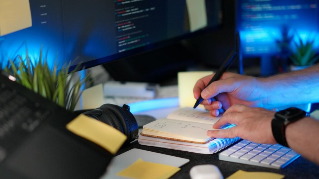 Hands using a laptop while checking items off a paper checklist.