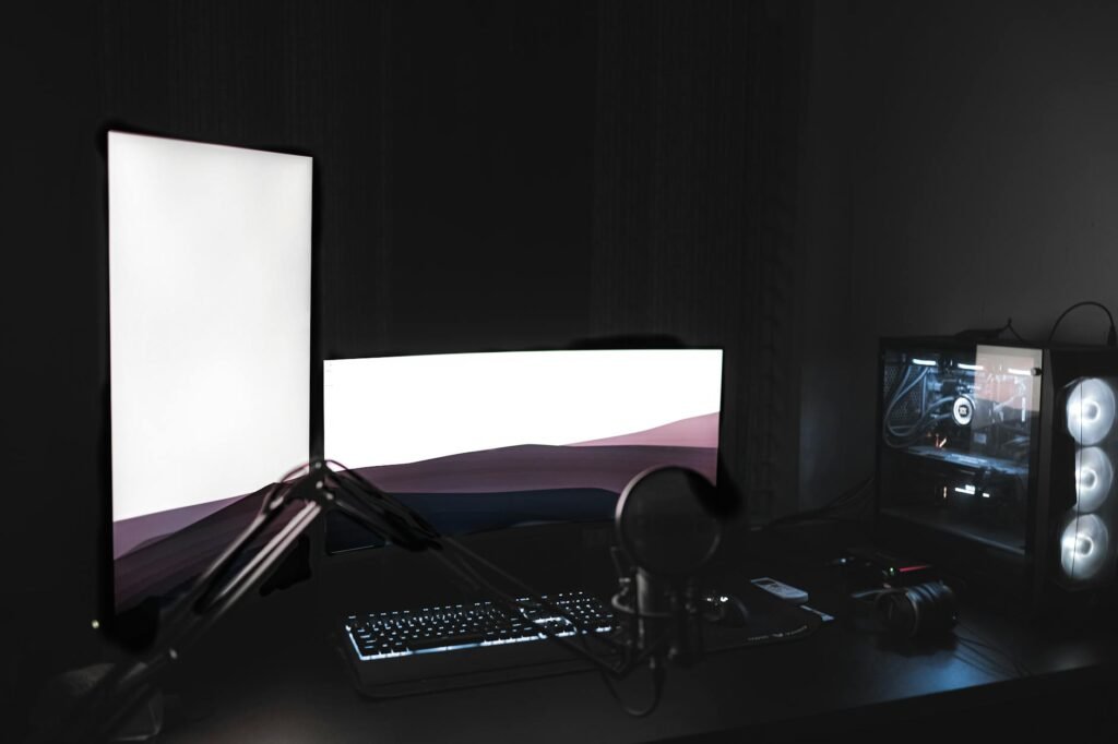 A dual-monitor PC workstation with a centered main screen, side display, microphone arm, and organized desktop