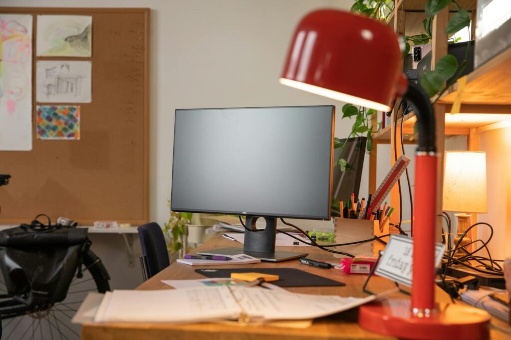 A desk lamp aimed at a notebook and keyboard beside a monitor, with no glare on the screen.